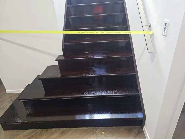 Dark timber staircase with newly coated treads and risers, taped off while drying