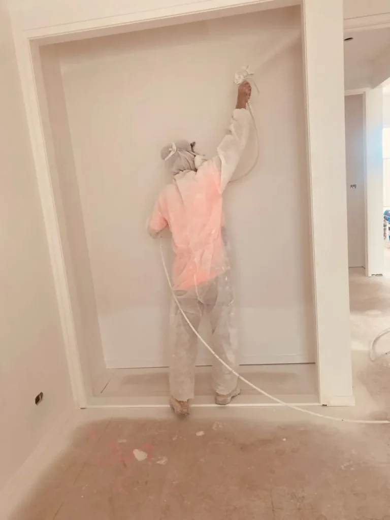 Austa painter in protective overalls spraying an interior wall